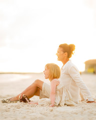 Happy baby girl and mother sitting on the beach in the evening