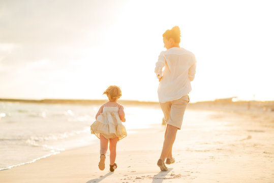 Mother And Baby Girl Running On The Beach In The Evening