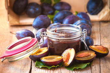 Jar of plum jam surrounded by plums on background wooden rural t
