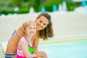 Portrait of mother and baby girl sitting near swimming pool