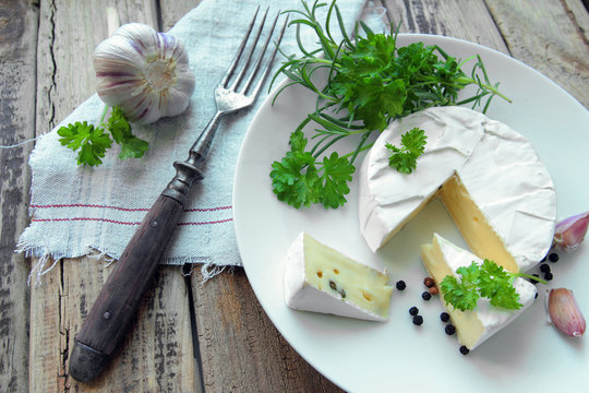 Fresh camembert cheese with herbs on a white plate with fork