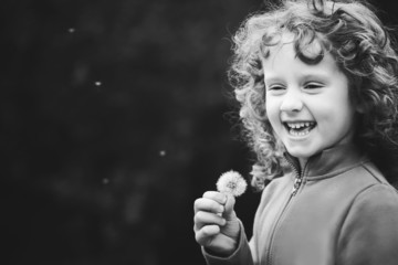 Beautiful little curly girl blowing dandelion, black and white p