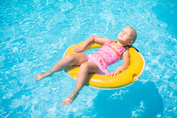 Adorable girl relax on yellow life ring in pool at protical beac