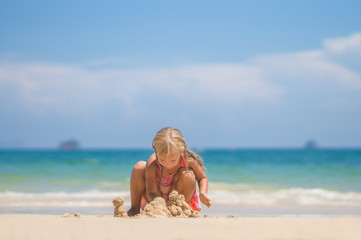 Adorable girl in pink swimming suit play on beach making sand to