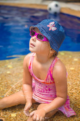 Adorable girl with pink sunglasses and blue hat sit in pool on s