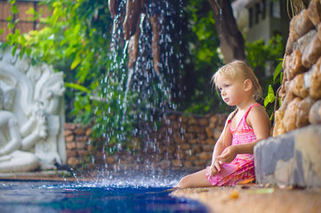 Adorable girl sit on pool side with small waterfall on back