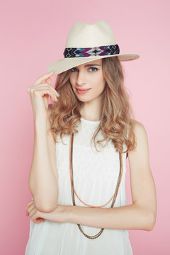 Beautiful woman in white dress posing on pink background in hat