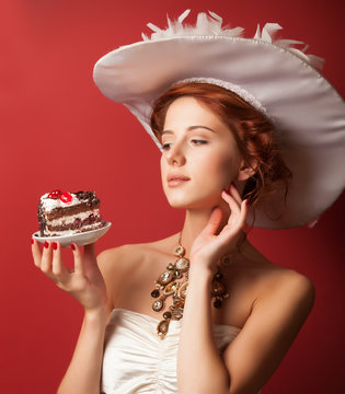 Portrait of redhead edwardian women with cake on red background.