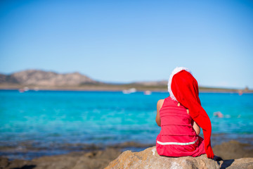 Adorable little girl in Santa hat and red dress sitting on big