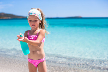 Little adorable girl in swimsuit with suntan lotion bottle