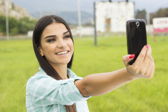 Portrait young girl taking selfies with her smart phone in park