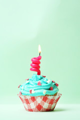 Delicious birthday cupcake on table on light green background