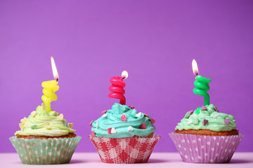 Delicious birthday cupcakes on table on purple background