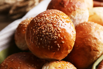 Tasty buns with sesame in wicker basket, on  wooden background