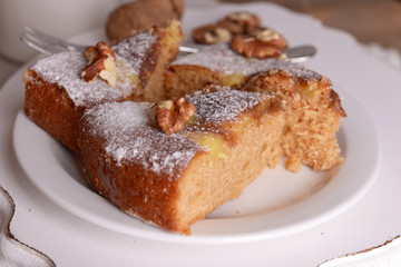 Pieces of delicious cake with nuts on plate on wooden table