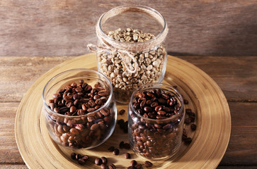 Coffee beans in jars on bamboo plate on wooden background