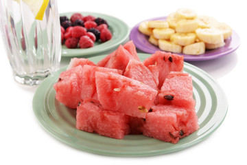Sliced fruits and berries on plate with glass of water close up