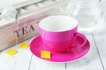 Cup and teapot with tea bags on wooden table close-up