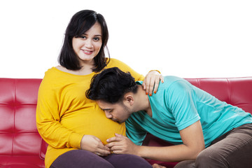 Husband kissing his wife belly on sofa