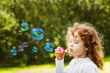 A little girl blowing soap bubbles, closeup portrait beautiful c