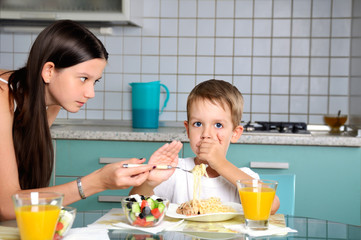 sister trying to feed her brother. he resists and repels fork wi
