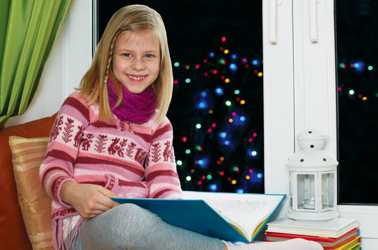 girl reading a book sitting on the window on Christmas Eve