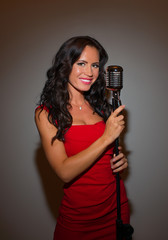 Attractive brunette woman singing into vintage microphone.