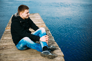 Young handsome man sitting on wooden pier, relaxing,  thinking,