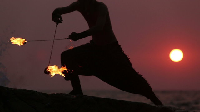 Male Artist of the spins fire poi on a rock 