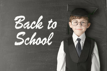 Cheerful little boy on blackboard. Looking at camera