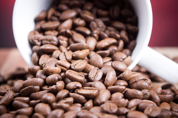 Coffee beans falling out of white mug.