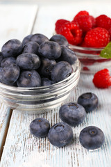 Glass bowls of raspberries and blueberries on wooden background
