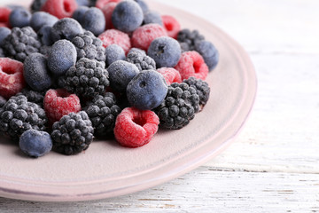 Iced berries on plate, on color wooden background