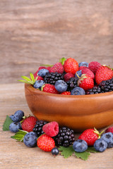 Ripe sweet different berries in bowl, on old wooden table