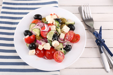 Greek salad served in plate on napkin on wooden background