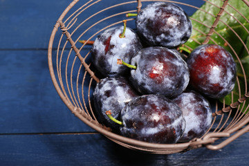 Ripe sweet plums in metal basket, on wooden table