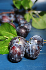 Ripe sweet plums with leaves, on wooden table