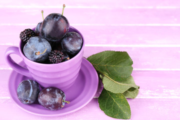 Ripe sweet plums in big cup, on pink wooden table