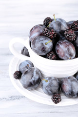 Ripe sweet plums in big cup, on grey wooden table