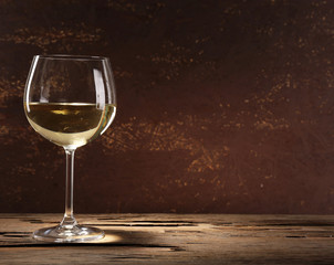 Goblet of white wine on wooden table on wooden wall background