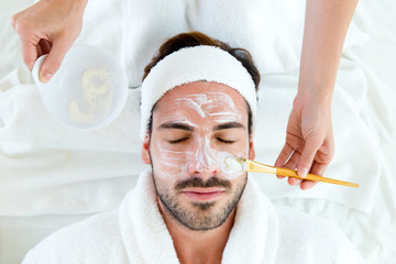 Man with clay facial mask in beauty spa.