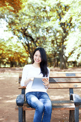 Obraz premium 公園のベンチでタブレットPCを使う女性