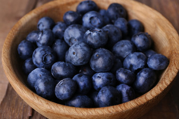 Wooden bowl of blueberries on wooden background closeup