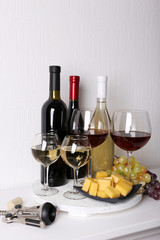 Obraz premium Assortment of red and white wine bottles with glasses, cheese cubes, and grapes on a white wooden tray