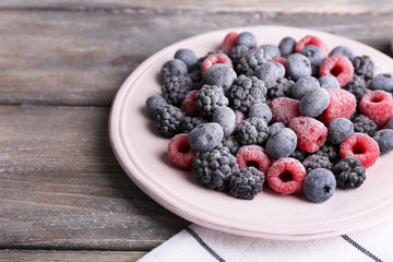 Iced berries on plate, on color wooden background