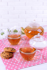 Teapot and cups of tea on table on brick wall background