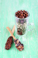 Glass and spoons with coffee beans on green wooden background