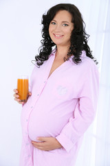 Young pregnant woman holding glass of juice on light background