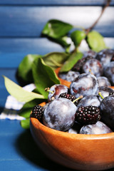 Ripe sweet plums in bowls, on wooden table