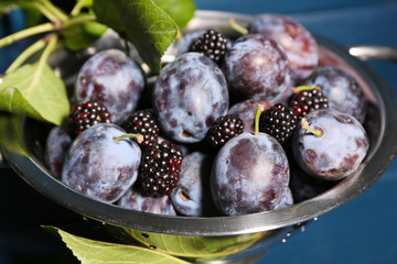 Ripe sweet plums in metal colander, on wooden table